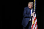 U.S. Republican presidential candidate Donald Trump hugs a U.S. flag as he takes the stage for a campaign town hall meeting in Derry, New Hampshire August 19, 2015.