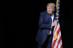 U.S. Republican presidential candidate Donald Trump hugs a U.S. flag as he takes the stage for a campaign town hall meeting in Derry, New Hampshire August 19, 2015.