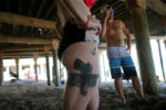 Laura Wallace and Jacob Alves stay cool under the Surf Side deck at Salisbury Beach in Salisbury, MA. She said her tattoos relate to the her father, "me and my dad used to go shooting and hunting together." She said she got the anchor because her father was a lobsterman and was often out to sea, "this is going to sound cheesy... he told me that when I missed him I could go to the beach and it would be like he was there and the breeze would be like a hug from him."
