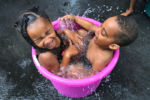 Devynn Minard 5 and her friend Tyler Tavares, 4, make the best with what they have, as they stay cool squeezing into a large bucket in Minard's driveway on Church Street during a heatwave in Boston.