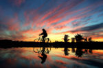 A bicyclist is reflected in a puddle in a parking lot at Scusset Beach in Boourne at dusk.