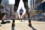 The prosthetics of Boston Marathon bombing survivor Celeste Corcoran frame a runner crossing the finish of the Boston Marathon as she waited for runners raising money for the group, 50 Legs to cross. Celeste lost both legs in the 2013 marathon bombing in the first bomb last which was 45 feet from the finsih line. Officials let her stand there to cheer on the the runners.