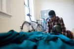 Liniște, a 22-year-old gay woman who is experiencing homelessness, makes her bed in her friend's apartment in Roxbury, MA, where she is staying temporarily.
