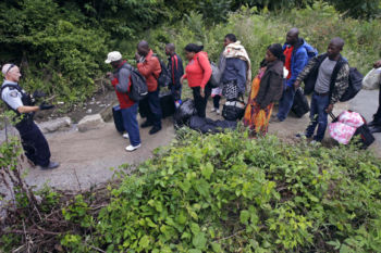 A Royal Canadian Mounted Police officer, left, standing in Saint-Bernard-de-Lacolle, Quebec, advises migrants that they are about to illegally cross from Champlain, N.Y., and will be arrested, Monday, Aug. 7, 2017. Officials on both sides of the border first began to notice last fall, around the time of the U.S. presidential election, that more people were crossing at Roxham Road. Since then the numbers have continued to climb.