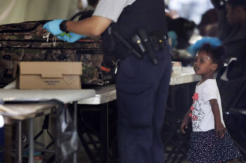A child watches as a Royal Canadian Mounted Police officer searches luggage from migrants who illegally crossed the border into Canada from New York at a makeshift police station in Saint-Bernard-de-Lacolle, Quebec.
