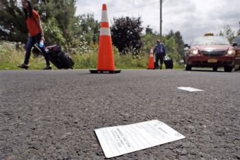 A bus ticket dropped by a passenger, who originated their travel in Jacksonville, Florida, is discarded on the pavement as migrants wheel their luggage down Roxham Road in Champlain, N.Y., while heading to an unofficial border station across from Saint-Bernard-de-Lacolle, Quebec.