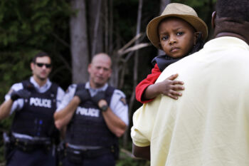 A Haitian boy holds onto his father as they approach an illegally crossing point, staffed by Royal Canadian Mounted Police officers, from Champlain, N.Y., to Saint-Bernard-de-Lacolle, Quebec, Monday, Aug. 7, 2017. Seven days a week, 24-hours a day people from across the globe are arriving at the end of a New York backroad so they can walk across a ditch into Canada.