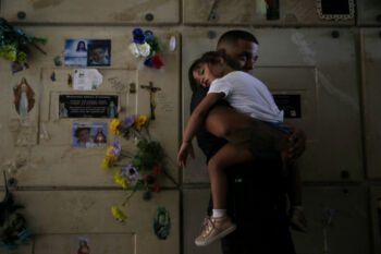 Corozal, Puerto Rico -- 10/02/2017 - Orlando Gonzalez holds his daughter, Nahielys, inside a mausoleum at their neighbor, Victor Ruiz's funeral. After the storm had knocked power out on the island, Ruiz had been using his car to charge the machine that helped him treat his emphysema. When he started to run low on fuel he went to a nearby gas station. He had waited over 35 hours in line when a nearby explosion sent a plume of smoke up into the air, causing the gas station to be evacuated. Ruiz made it home, but died in his car before he could get out. The death count has not included people like Ruiz, whose death was an indirect result of Hurricane Maria.