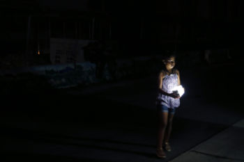 San Juan, Puerto Rico -- 10/01/2017 - A child forced onto the street with her family to escape the heat inside their public housing apartment held onto one of the few sources of light along this darkened stretch of city in a blacked out San Juan. Nearly four months after Hurricane Maria first made landfall an estimated 40 percent of Puerto Rico is still in the dark.