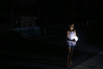 San Juan, Puerto Rico -- 10/01/2017 - A child forced onto the street with her family to escape the heat inside their public housing apartment held onto one of the few sources of light along this darkened stretch of city in a blacked out San Juan. Nearly four months after Hurricane Maria first made landfall an estimated 40 percent of Puerto Rico is still in the dark.