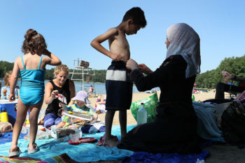 The Last Refugee: Through the Closing Door
7. AsmaaÕs first visit to an American beach was fraught for her and for volunteer Jessica Lassiter. How would a conservative Muslim feel surrounded by Americans in bathing suits? Asmaa stood out in her long coast and head scarf. Would people judge her by how she was dressed? At first Asmaa stayed anchored on the blanket in a shaded nook at Walden Pond, staying busy by setting out her home made Middle Eastern dishes. Eventually, she left the shade and walked barefoot to the water, lifted the hem of her coat and stood in the cold water.Ê