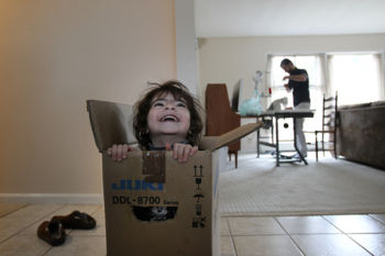 The Last Refugee: Through the Closing Door
8. Abdulkader set up his new professional-grade sewing machine as his daughter Ameeneh played in the box it arrived in. The machine was purchased with donations from a local mosque.
In Syria, he had a thriving tailoring shop for just a year when the war began. Overnight, the city he loved began to disappear, its homes, hospitals, and historic monuments devastated by bombs, fires, and looting, and he understood with dread that he and his family would have to leave.
In another country, Jordan, he began again. For a time, before his family joined him, he was homeless, sleeping at night in the workshop where he labored. When he saved enough to send for Asmaa and the children, they moved into an old refugee camp, its stark, stone housing units cheap and rough and bare.
Now, five years later, in America, he was crouched over the starting line once more. In two days, Abdulkader would turn 30. How many times would he have to start from nothing?