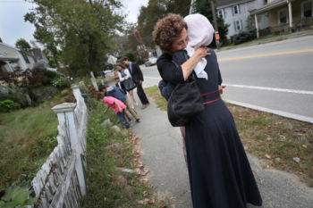 The Last Refugee: Through the Closing Door
11. Jewish volunteer Bonnie Rosenberg hugs Amsaa Hayani on Yom Kippur, the holiest of Jewish Holidays as the walk to the temple for a special blessing by the rabbi.
The Hayani family had arrived in Boston on a rainy night in January eight months earlier, and had been stunned by the warmth of the welcome they found. And then they had been stunned to learn, soon after their arrival, that the people helping them were Jewish. They had been taught that Jews were their enemy. For a time it made them anxious. Volunteers from the temple in Wellesley were at the house almost every day; they took the family shopping and to appointments and playgrounds. Their children bonded. With their nurturing support, the refugees began to make their way, and come to learn they were taught an untruth. In September, on Yom Kippur, the eight Syrian families were welcomed to Temple Beth Elohim. Asmaa, surrounded by her new Jewish friends, stood on the bimah after thanking the congregation for their love, support, and new lives.