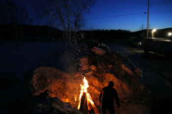 Allagash, ME -- 3/5/2017 - Spectators outside of the Allagash checkpoint build a fire to keep warm as mushers arrive and take off in spurts. It takes days to complete the race, with mushers resting at mandatory intervals and then heading back into the bitter cold to harness their dogs.