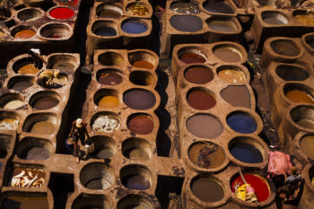 Located within a UNESCO world heritage site, the Chouara tannery is considered to be among the oldest in the word still in operation. For over a thousand years leather goods have been produced and sold at this site using only traditional methods of production. Hides are processed and softened in wells that are filled with a white liquid, which is a mixture of pigeon feces, donkey urine, salt, and water. They are then beaten to a pulp by hand and foot before they are colored in surrounding vats which are filled with dyes. While it is extremely difficult to navigate the Medina in Fes, you can tell when you are nearing the tannery due to the distinct smell the site gives off.
A worker carries vats of liquid between dying wells at the Chouara tannery in the Medina in Fes, Morocco on July 28, 2017.