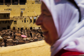 A woman looks on from the roof of a surrounding leather shop as workers operate inside the Chouara tannery below in the Medina in Fes, Morocco on July 29, 2017.