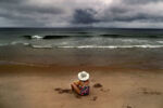 The arm of Cape Cod has challenged the power of the sea for centuries, but the contest has escalated. Climate change is altering this vacation paradise in myriad ways, perhaps forever. The waves crash like they always do, but they are not the same. They come from the open ocean now. Families play on beaches that look like they always have, but the sand is not the same either. To see what is happening on the Cape, you have to know where to look. Tody's storms and sea tear up the marsh and the shore. Homes along the coast are in danger. A warmer atmospher holds more water vapor providing more fuel for storms and hurricanes.
Salome Verkoville, 10 from Boston sits on Nauset Beach in Orleans as ominous strom clouds hang in the distance.The beach has been in the cross hairs of many storms, and erosion has taken a prt of it over the last decade.