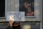 A woman and a girl watch from window as demonstrators pass by protesting against racial inequality in the aftermath of the death in Minneapolis police custody of George Floyd in Salem, Massachusetts, June 12, 2020.