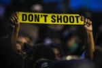 BOSTON - 6/2/2020: A protester holds up a piece of yellow plastic that reads "don't shoot" while participating in a demonstration outside of the Forest Hills T Station. The rally and vigil took place on Blue Ave by Franklin Park to honor George Floyd, Breonna Taylor, Ahmaud Arbery and local fallen people. The demonstration was organized by Black Lives Matter Boston and Violence in Boston.