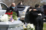 Everett, MA - 4/29/20 - Family members embrace as other mourners look on from the car during the funeral service for Santos A. Rivas at Woodlawn Cemetery in Everett. Due to strict social distancing guidelines only ten people are allowed outside of the car for graveside services at Woodlawn Cemetery in Everett. Friends and family lined three sides of the street surrounding the gravesite to pay their respects to Santos A. Rivas, who passed away from coronavirus or COVID-19.