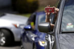 Everett, MA - 4/29/20 - A mourner holds a cell phone out to record as she attends Santos A. Rivas' funeral from inside her car. Due to strict social distancing guidelines only ten people are allowed outside of the car for graveside services at Woodlawn Cemetery in Everett. Friends and family lined three sides of the street surrounding the gravesite to pay their respects to Santos A. Rivas, who passed away from coronavirus or COVID-19.