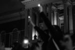 A police officer watches from the Massachusetts Statehouse balcony as protesters hold up their lit phones at a vigil for victims of police brutality on May 31, 2020.