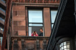 A person uses binoculars to watch people at a Black Lives Matter protest outside the Massachusetts Statehouse from her window on May 29, 2020.