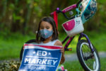 A young girl sits by her bicycle and holds an Ed Markey sign in Acton, Massachusetts on Aug. 8, 2020.