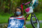 A young girl sits by her bicycle and holds an Ed Markey sign in Acton, Massachusetts on Aug. 8, 2020.