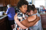 SYNOPSIS: A Marlborough, MA nonprofit caring for and teaching skills to people with developmental and intellectual disabilities couldn’t fill positions for years. But after they learned that Haitian migrants at a shelter in a nearby Econo Lodge had received work authorization, the leadership at Thrive Support and Advocacy sought to hire them, allowing them to expand their programs. Many of the people hired stayed close, attending social events and living in the same apartment buildings.
Sindy Micourt hugs resident Kristen Camacho at the Thrive Support and Advocacy center in Marlborough, MA on August 14, 2024. Camacho was stressed about her irritated eye.